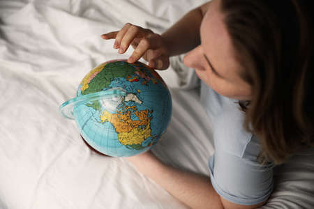 Close-up portrait of woman laying in bed and holding globe. Horizontal.の写真素材