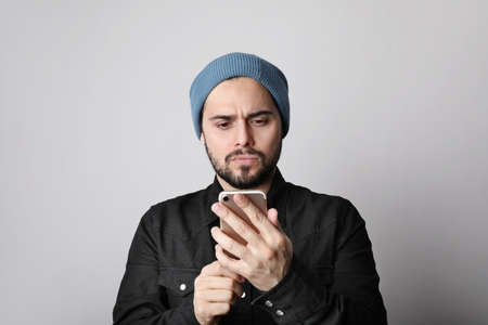 Handsome and bearded hipster wearing stylish hat on head. Brutal man with mustache and beard using his smartphone.の写真素材