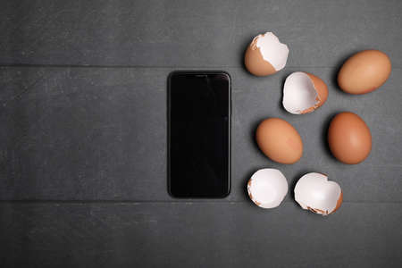 Raw chicken eggs and black smartphone on wooden table. Space for text.の写真素材