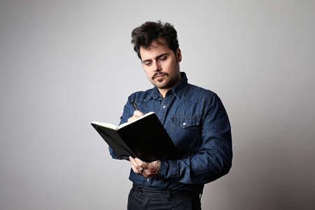 Modern young man hipster with a book and wearing a stylish denim shirt. Attractive guy in fashionable clothes.の写真素材