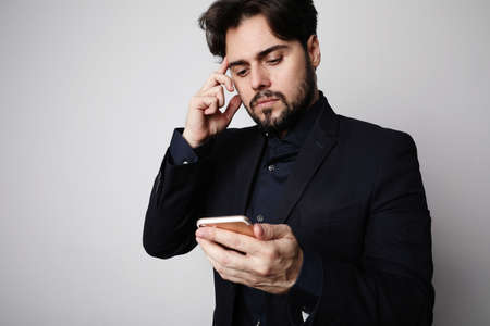Serious bearded businessman using smartphone in suit on the white background.の写真素材