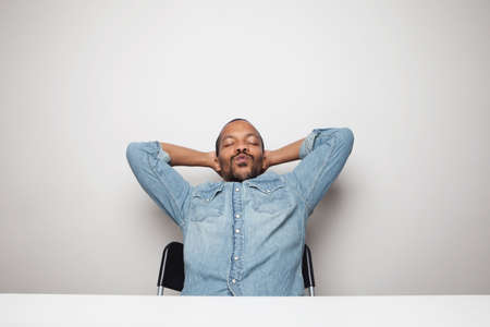 Portrait of young black man wearing denim shirt against white wall with happy face.の写真素材