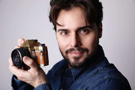 Close-up portrait of young bearded man with taking photos using vintage camera, isolated over white...