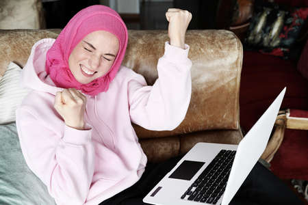 Portrait of young woman wearing muslim hijab working with her laptop computer with emotional face.の写真素材
