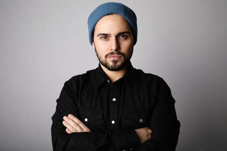 Side portrait of bearded hipster wearing blue hat and shirt looking at camera.