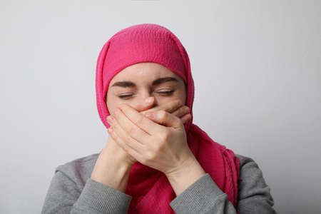 Young Muslim girl wearing a veil, covering her mouth with her both hands and crying, standing on a...