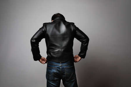 Portrait of man wearing leather jacket stands back in the studio.