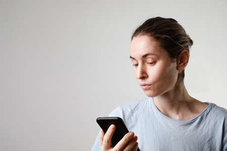 Lifestyle headshot woman on phone texting text message on smartphone app indoor. Caucasian female model in her 20s.の写真素材