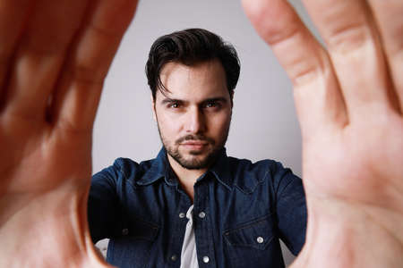 Close up of young bearded man with hand keeps close to camera, isolated over white background.の写真素材