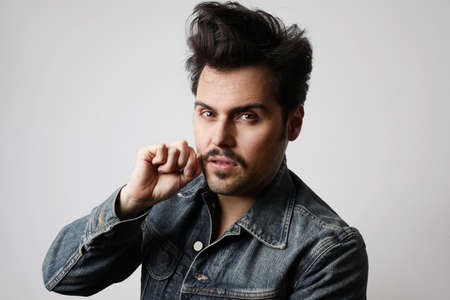 Headshot of serious stylish hipster looks straight with confident expression, wears denim jacket,...