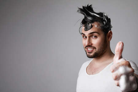 Happy bearded man with thumbs up while washing his hair. Men care concept.