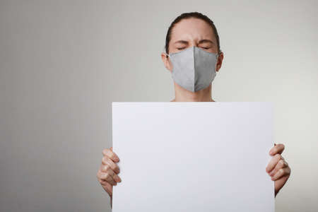 Close-up portrait of young woman in medical face protection mask with white banner. Pandemic...