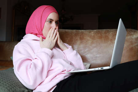 Portrait of a muslim woman working with computer and touching her face wearing a head scarf....