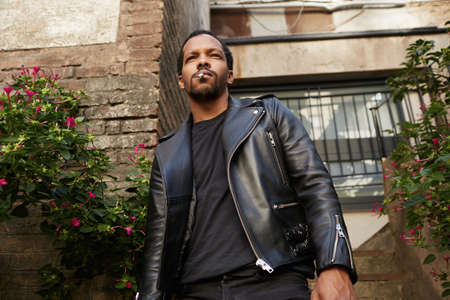 Outdoor portrait of smiling young African man wearing biker leather jacket. Handsome and confident.