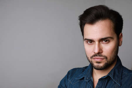 Portrait of 30-year-old man standing over grey background in denim shirt. Close up. Copy-space....