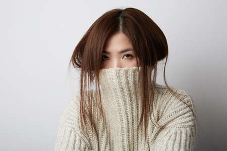Portrait of beautiful asian woman. Hiding her face in warm sweater .She is catching hair.の写真素材