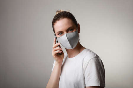 Close-up woman in medical face protection mask indoors on white background using her smartphone. Protection of the virus.の写真素材