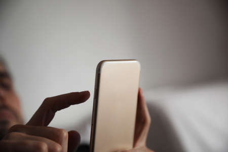 Mock-up of man using smart phone in bed. Relaxing after work. Space for text.