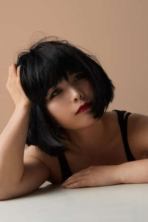 Vertical shot of beautiful asian woman with long hair and emotional face posing in studio on beige background. Isolated.の写真素材