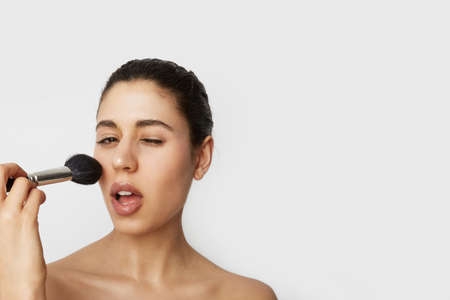 Close-up portrait of young beautiful woman doing nude make-up posing over white wall. Beauty concept.の写真素材