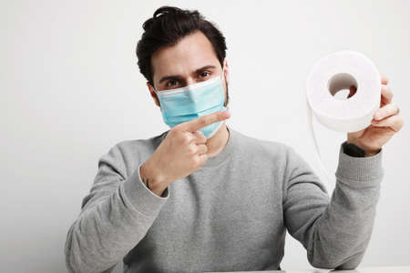 Excited caucasian man in medical mask is happy to have a stock of toilet paper. Stay at home.の写真素材