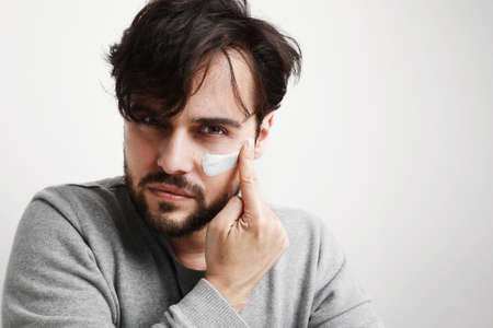 Close-up shot of attractive man with healthy skin, applies cream for anti wrinkle or anti aging,...