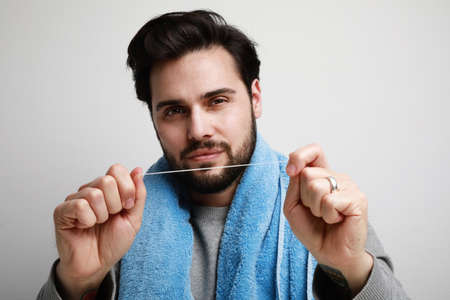 Close up bearded young man using dental floss isolated on grey background studio portrait....