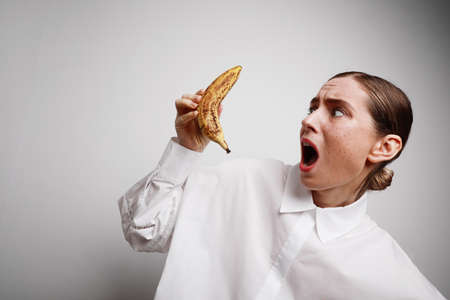 Young woman holds a spotted banana. Deadline time. Challenge.の写真素材