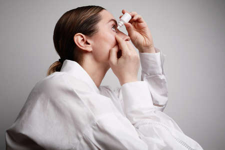 Woman with injured eye inserting eye-drop. Health care and eyesight concept. Conjuctivitis. Woman with injured eyeの写真素材