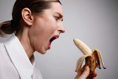 Young woman holds a spotted banana isolated over white background. Deadline time. Challenge.の写真素材