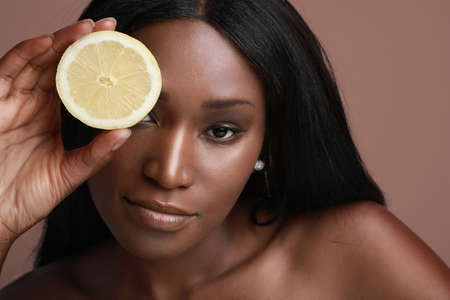 Close-up photo of beautiful dark skin model lady holding slice of citrus vitamin c fruit isolated brown background.の写真素材