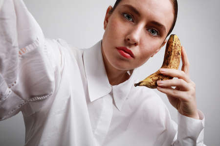 Young woman in casual clothes making fun with a banana on white background.の写真素材