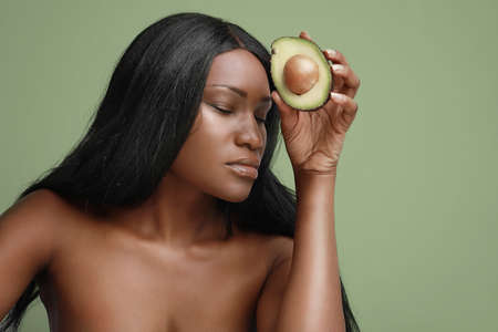 Close-up portrait of black young woman holding slice of avocado. Healthy way of lifestyle.の写真素材