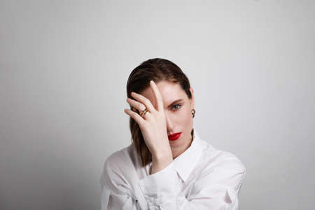 Attractive young woman wearing white shirt and red lips, touching her face, looking at the camera....