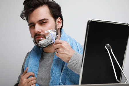 Handsome bearded man in casual clothes iwith beard apply shaving foam posing on gray background,