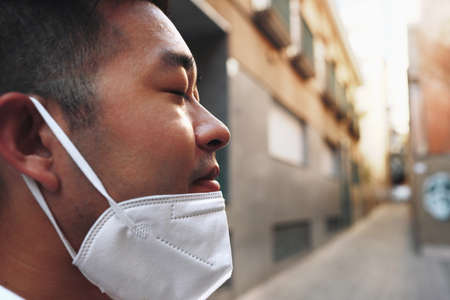 Street headshot of asian young man who is moved on a medical mask to bathe fresh air. Coveid-19,...