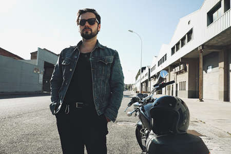 Headshot.of man wearing jeans jacket and sunglasses riding cafe racer motorcycle on a dusty dirt place.の写真素材