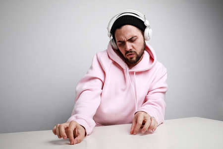Music everywhere. Funny bearded young man dancing and clapping. Wearing huge earphones and hoodie....