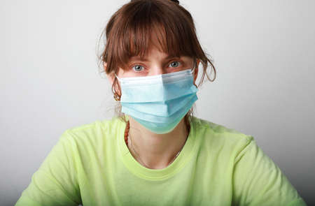 Cheerful young woman wearing medical mask sitting at her workplace. Space for text.