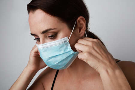 Close-up of young caucasian brunette woman using medical mask. Stay home. Pandemic situation.