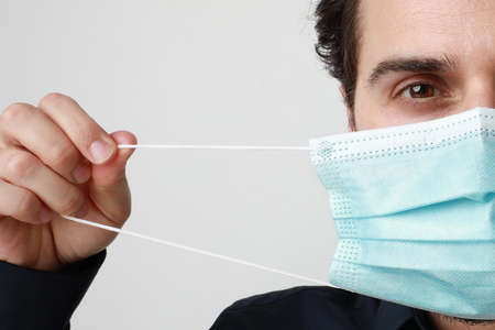 Cropped portrait of young man in medical mask, stands on light background. Pandemic situation,...