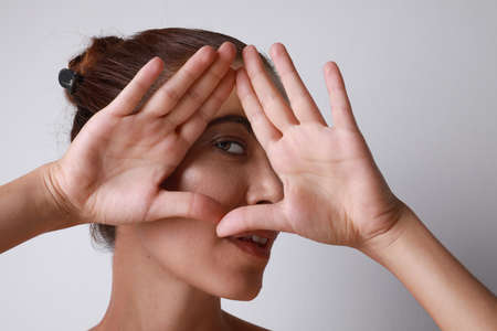 Young Woman shows gesture with fingers. Portrait of smiling lady posing over light background. Happiness and love.の写真素材