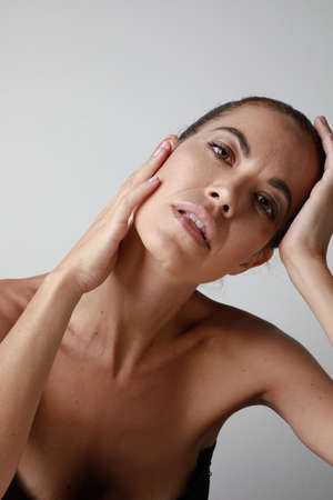 Vertical portrait of beautiful senior woman touching her skin isolated over grey background. Aging process concept.の写真素材