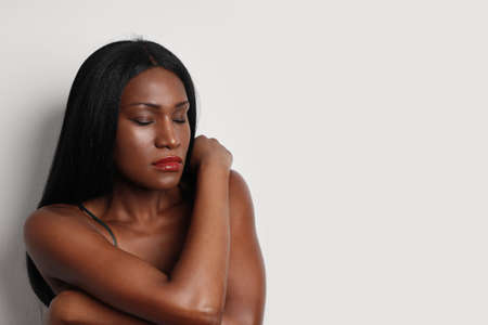 Close-up portrait of black woman with closed eyes and long hair and evening dress, posing on white background wall.の写真素材