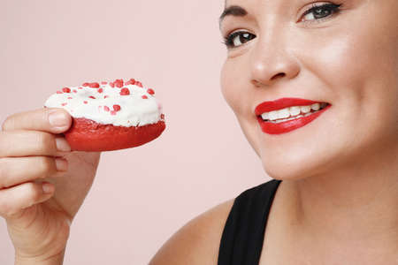 Close-up portrait of young happy woman holding tasty donut, posing over pink background.の写真素材