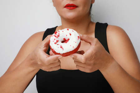 Close-up of young happy woman holding tasty donut, posing over white background.の写真素材