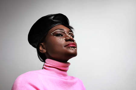 Young black woman with small pearls on her skin, posing over white background. Creative make-up.