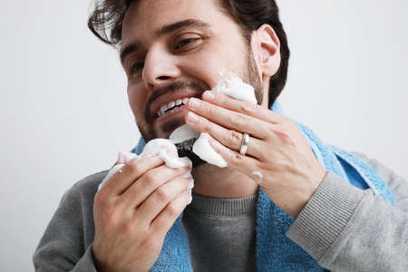 Happy bearded young man, shaving in the morning. Isolated on white background.