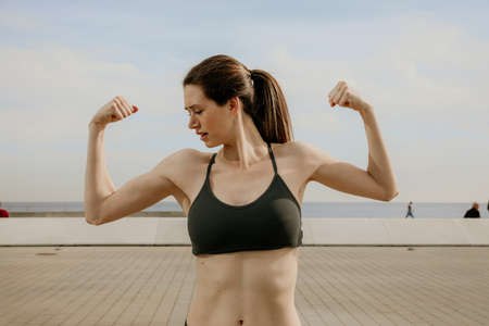 Portrait of young sporty woman showing biceps posing outdoor.の写真素材