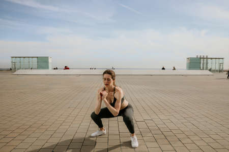 Woman with perfect body doing squats outdoor. Horizontal.の写真素材